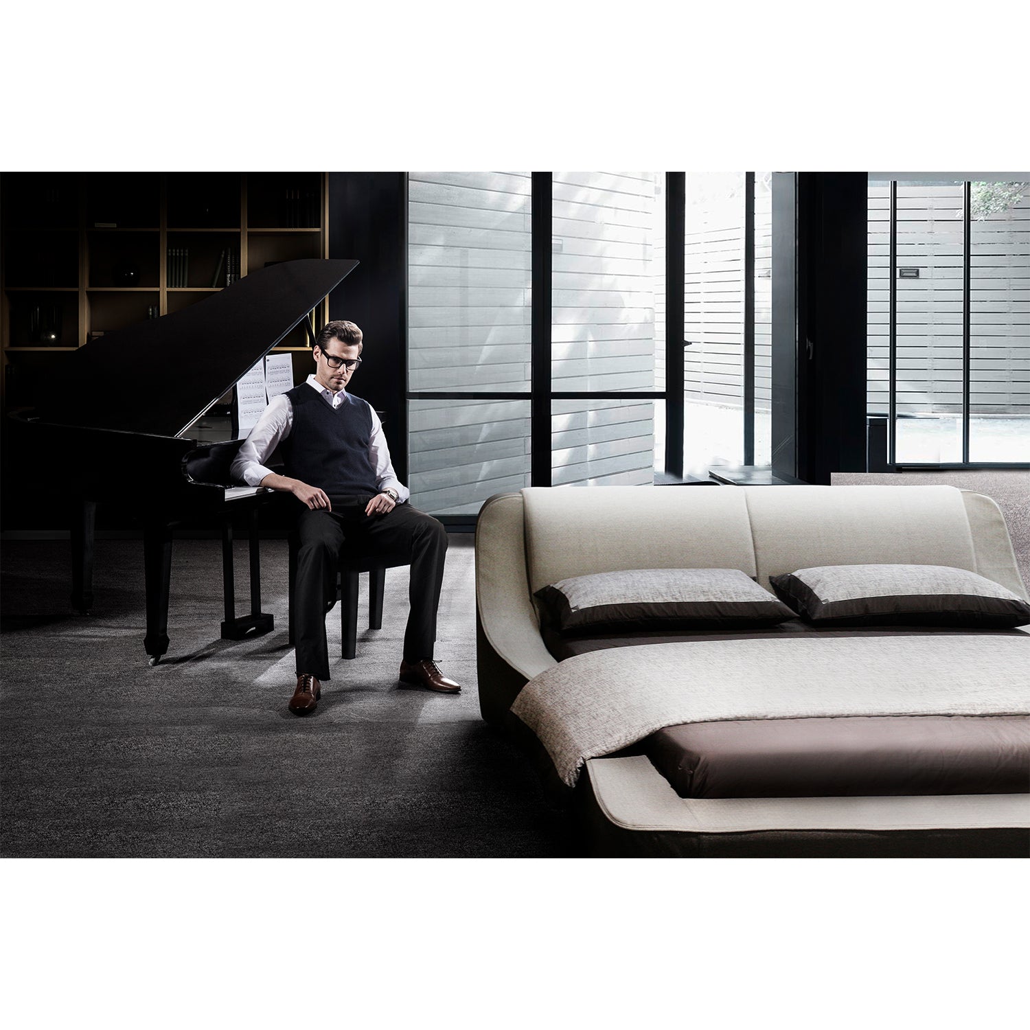 Elegant bedroom interior with a man sitting next to a grand piano and a modern white leather bed frame featuring brown pillows and bedding.