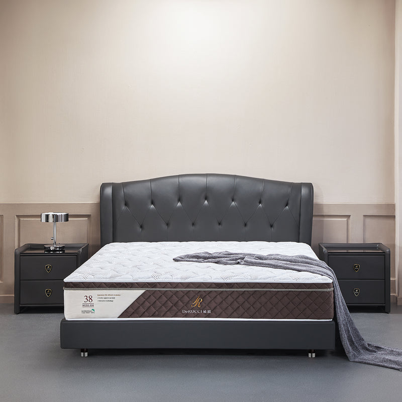 Modern bedroom setup with a black leather bed frame and tufted headboard, DeRUCCI Neuroscience Energy Mattress, and two black nightstands with chrome lamps. Grey blanket draped on the bed.