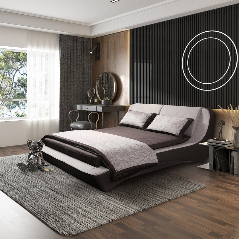 Modern bedroom featuring sleek black and white bed frame with monochrome bedding, dark vertical line back wall, circular wall decorations, gray area rug, nightstand with lamp and books, and a desk with chair.